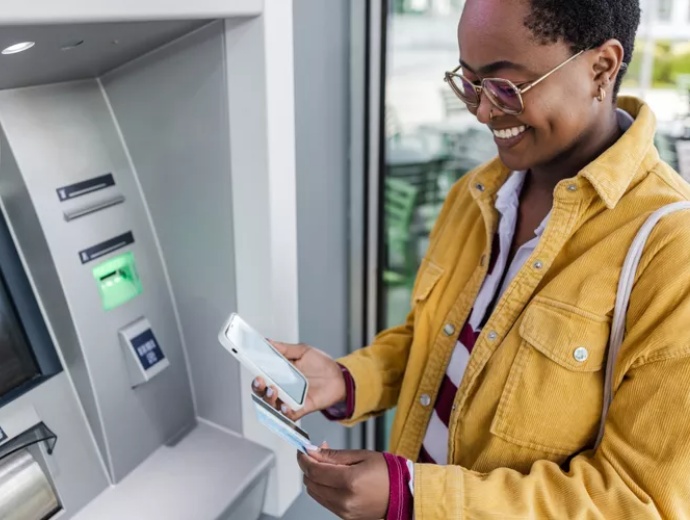 a woman holding her mobile phone at an ATM machine